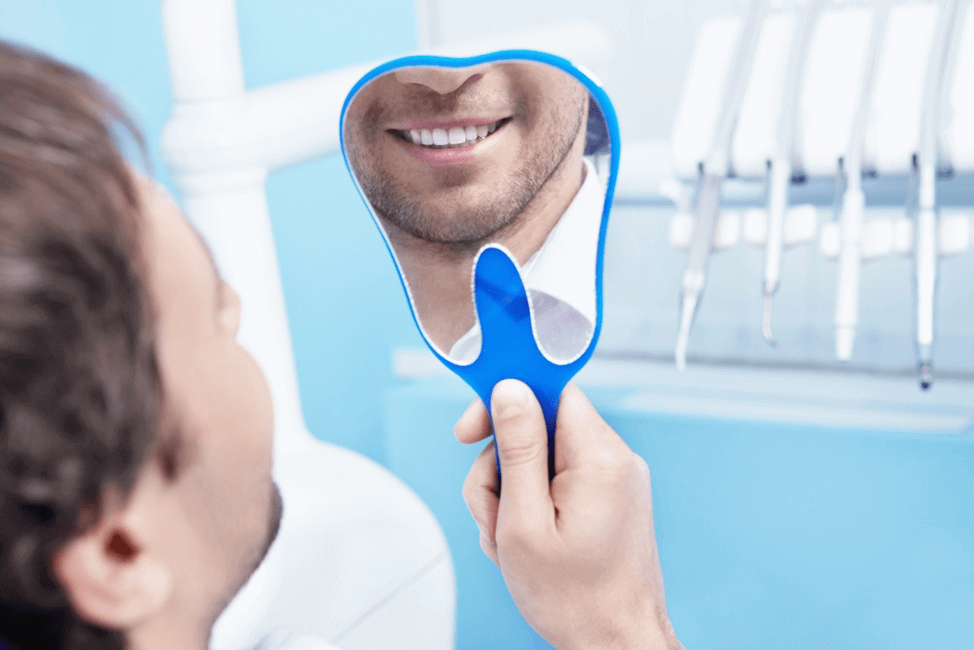 Patient in a dentist office checking his teeth with a mirror