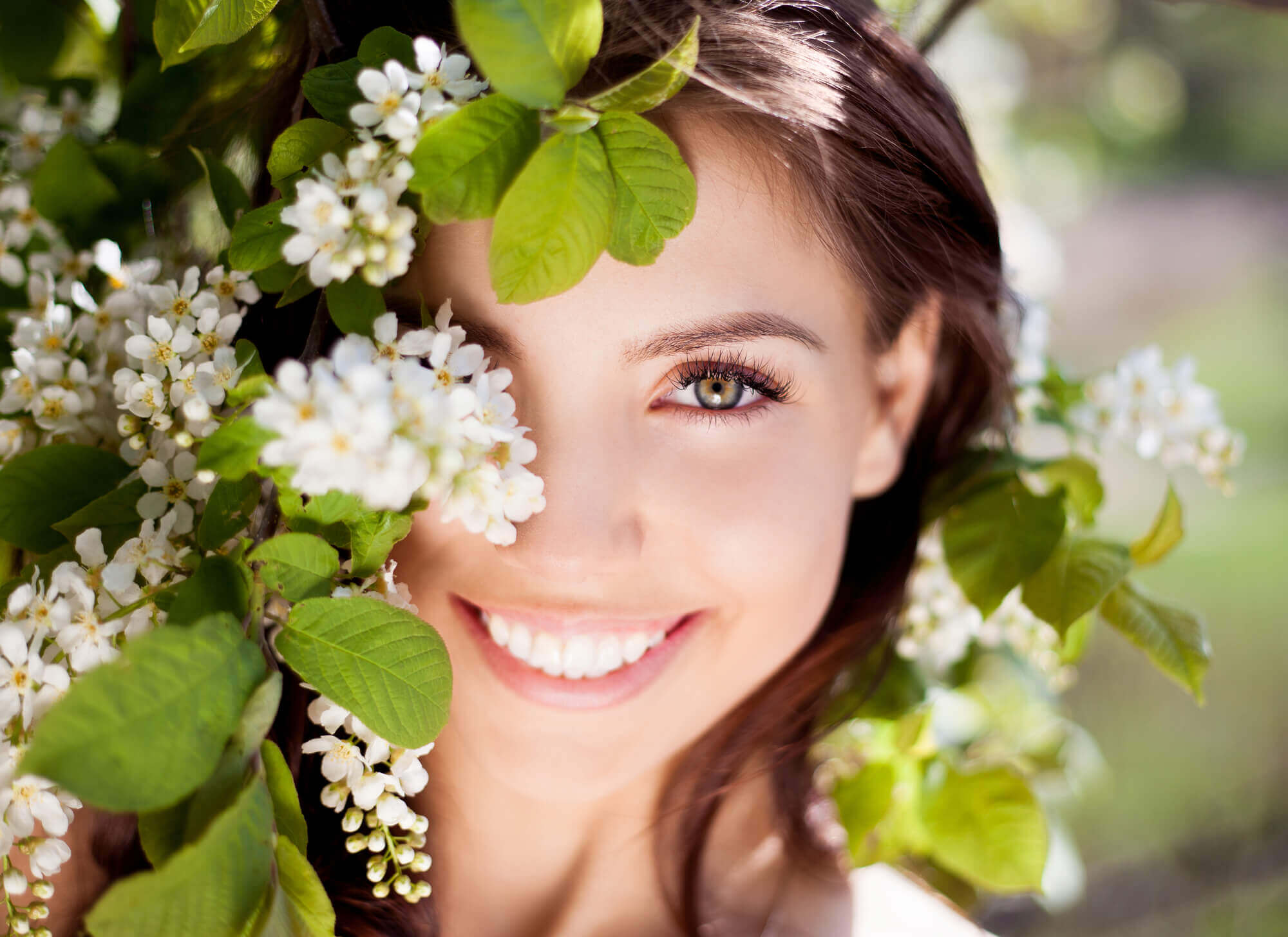 Young woman smiling while hiding behind white flowers 1