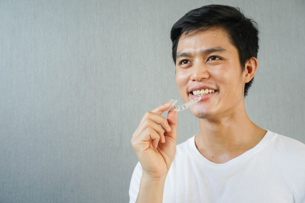 Close up Young Asian Man Smiling With Hand Holding Dental Aligner Retainer 
