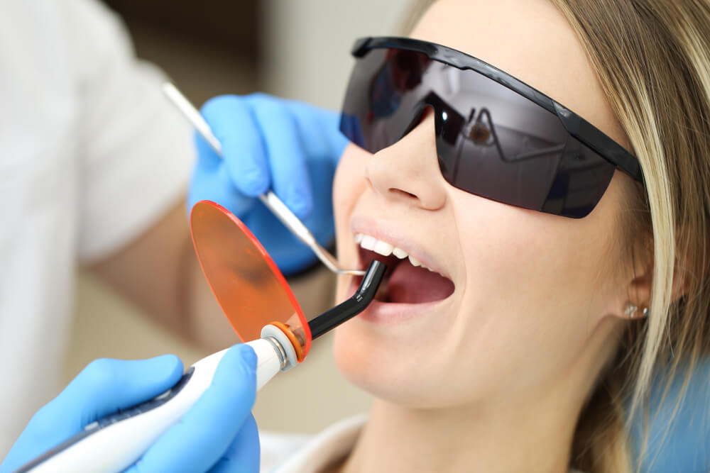 Blond Woman Wearing Black Glasses Being Examinated by Stomathologist With Uv. 